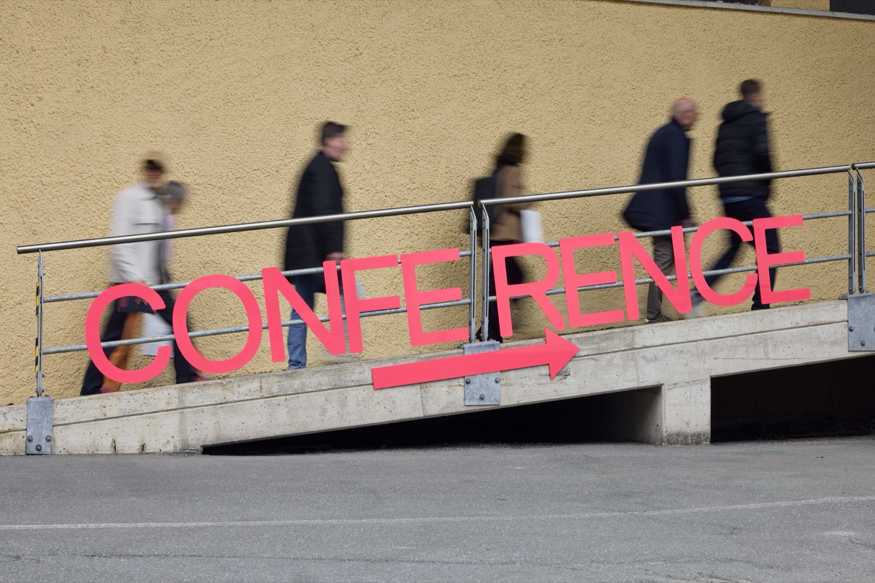 Besucher gehen an einem pinken Conference-Schriftzug vorbei