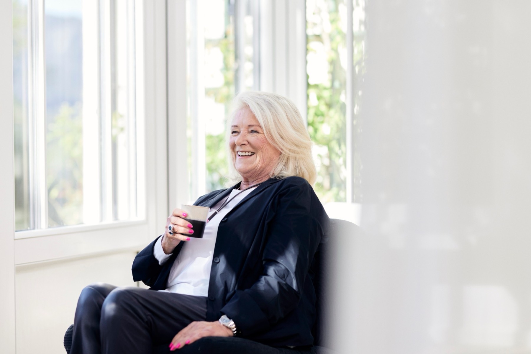 Lachende Frau mit Tasse am hellen Fenster