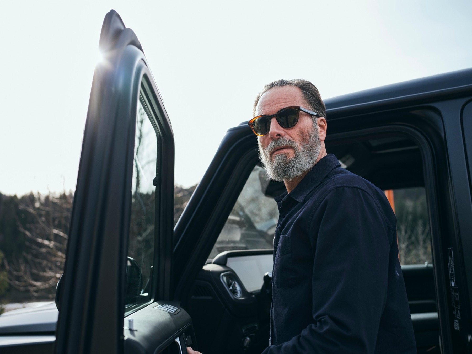Mann mit Sonnenbrille und grauem Bart an einer offenen Autotür